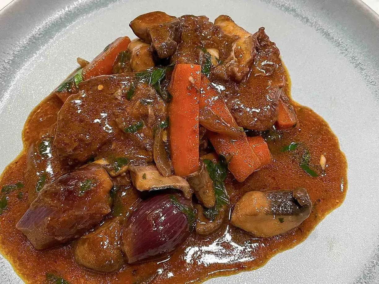 En mustig coq au vin med m&ouml;ra k&ouml;ttbitar, mor&ouml;tter, champinjoner och r&ouml;dl&ouml;k i en rik s&aring;s.