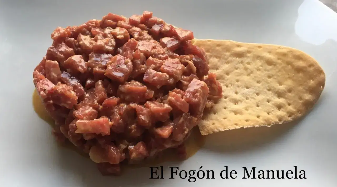 Delicioso tartar de salchichón picado finamente, servido sobre una base cremosa y acompañado de una galleta crujiente. ¡Una explosión de sabor!