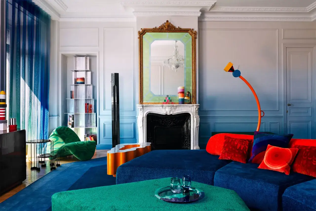 Salotto con arredamento parigino audace: divano blu, poltrona verde, specchio dorato e lampada arancione.