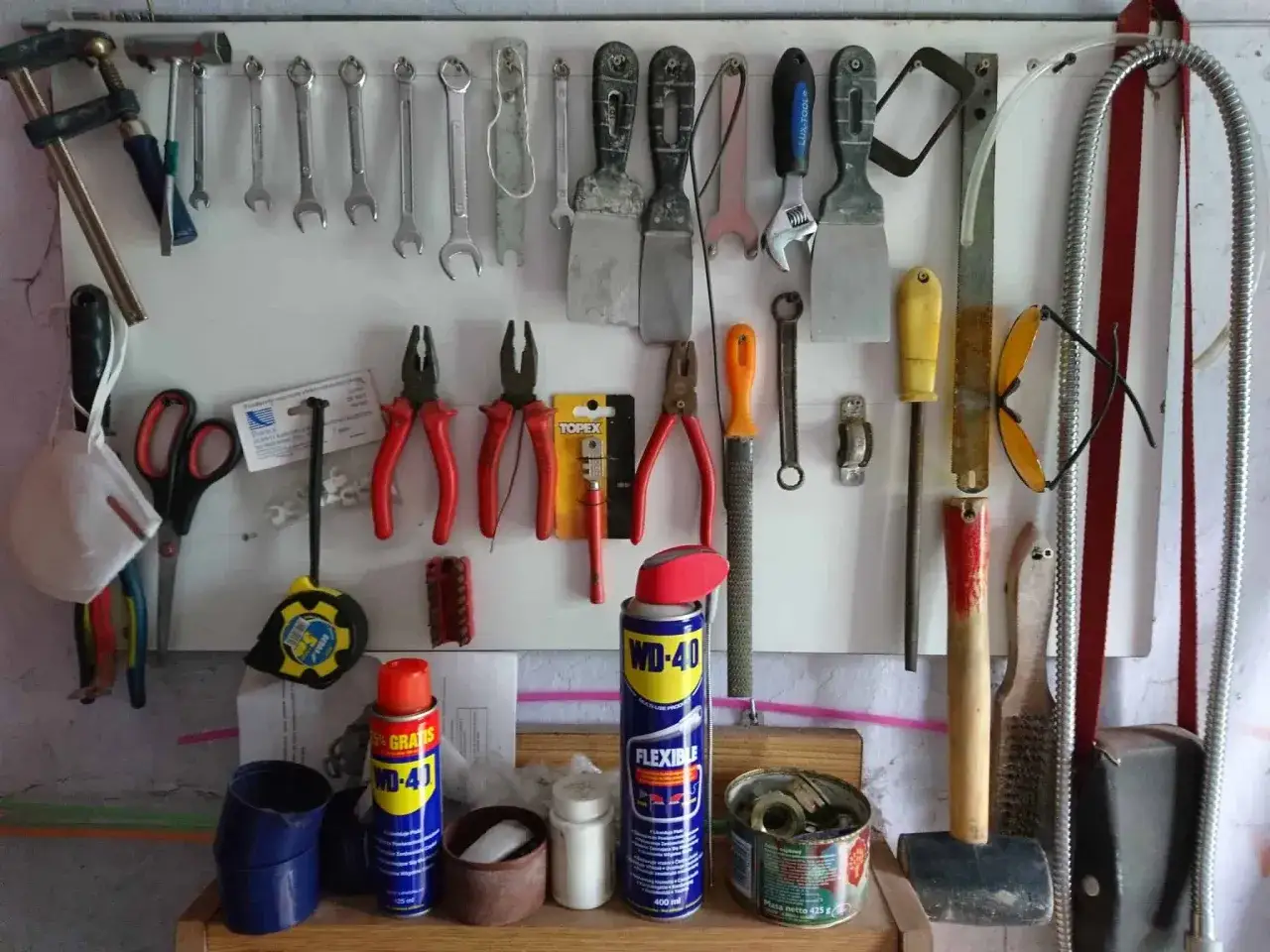 Narzędzia wiszące na ścianie, w tym klucze, śrubokręty, szczypce i puszka WD-40. Zastosowanie WD-40 jest szerokie, od smarowania po usuwanie rdzy.