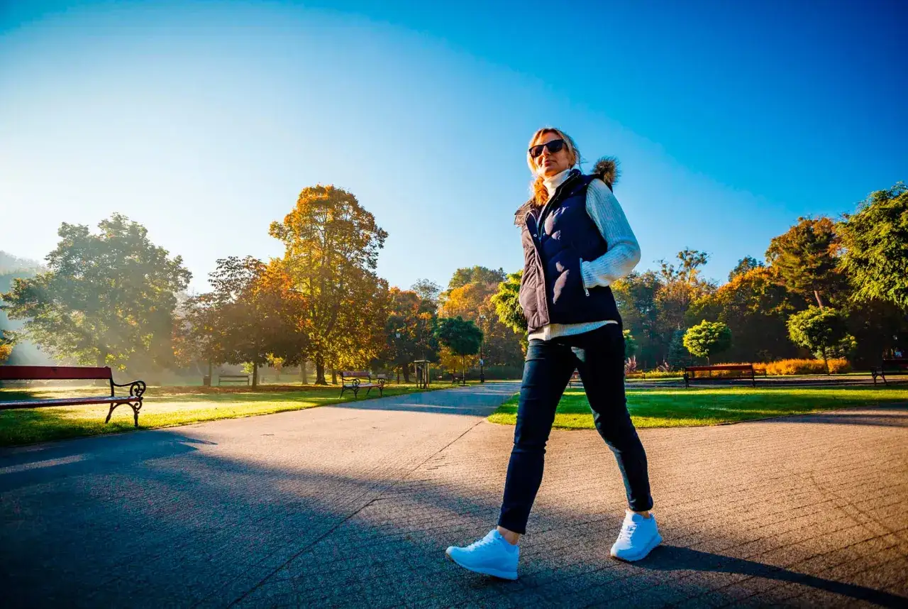 En kvinna promenerar i en park under h&ouml;sten, njuter av livet i solskenet.