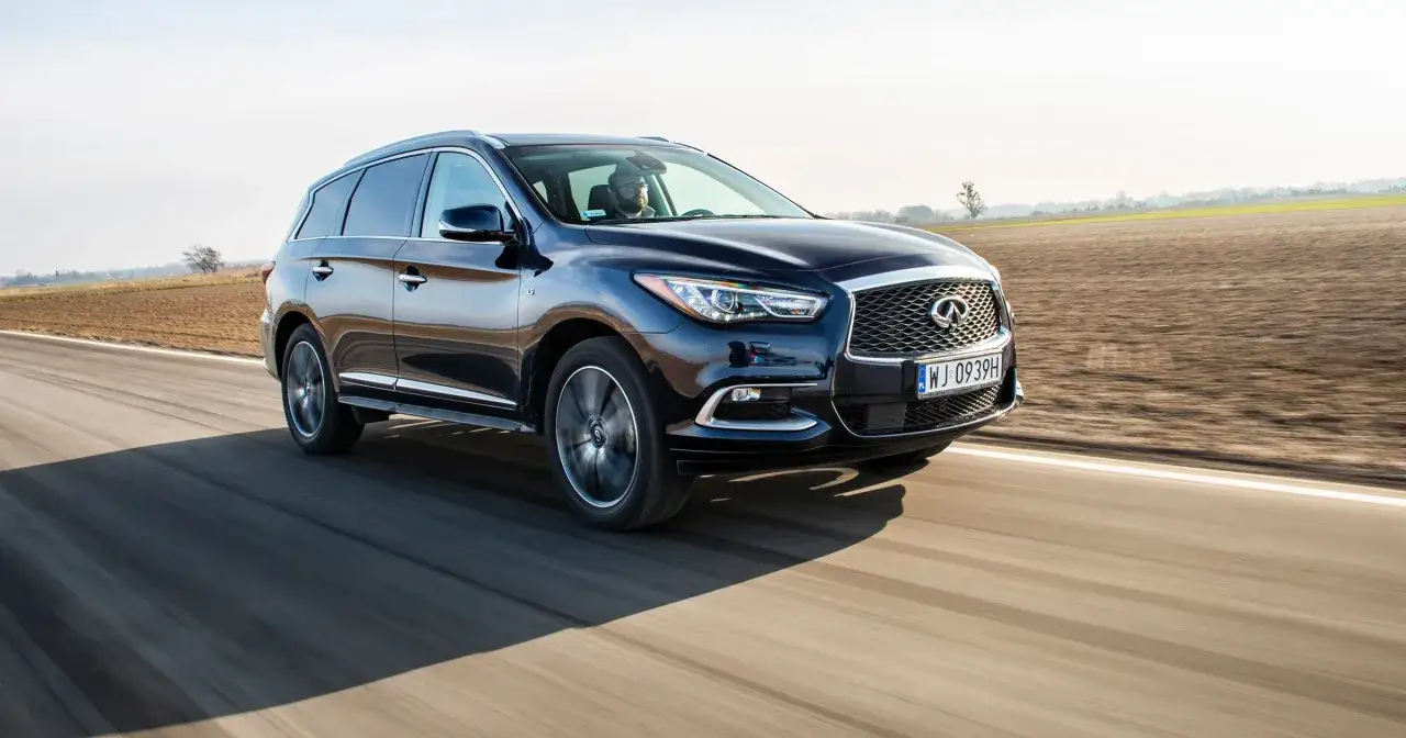 Ciemnoniebieski Infiniti QX60 jedzie po pustej drodze wśród pól.