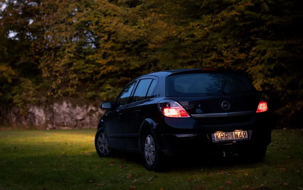 Czarny Opel Astra 2005 na trawie, w tle jesienne drzewa.