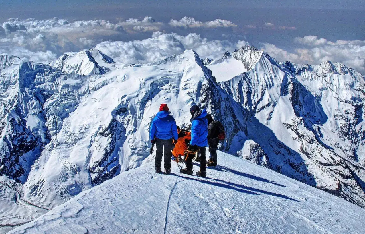 Trzej alpiniści stoją na ośnieżonym szczycie, podziwiając majestatyczne widoki na Mera Peak.