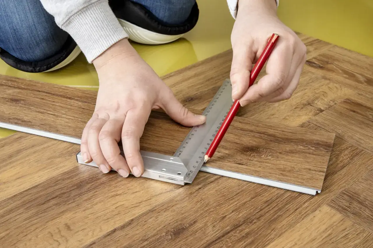 Mani che segnano con matita e squadra un pannello per la posa del laminato.