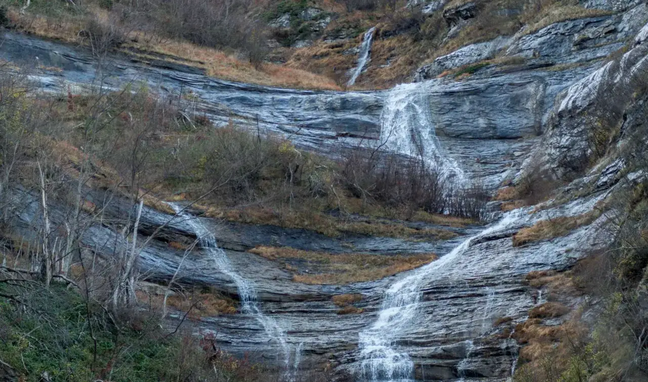 Le cascate della Volpara scendono su rocce stratificate, circondate da vegetazione autunnale e alberi spogli.