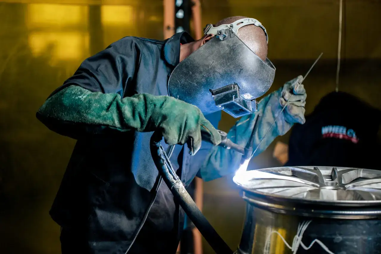 Soldador experto trabajando en cómo reparar llantas de aluminio, con equipo de protección y herramienta de soldadura.