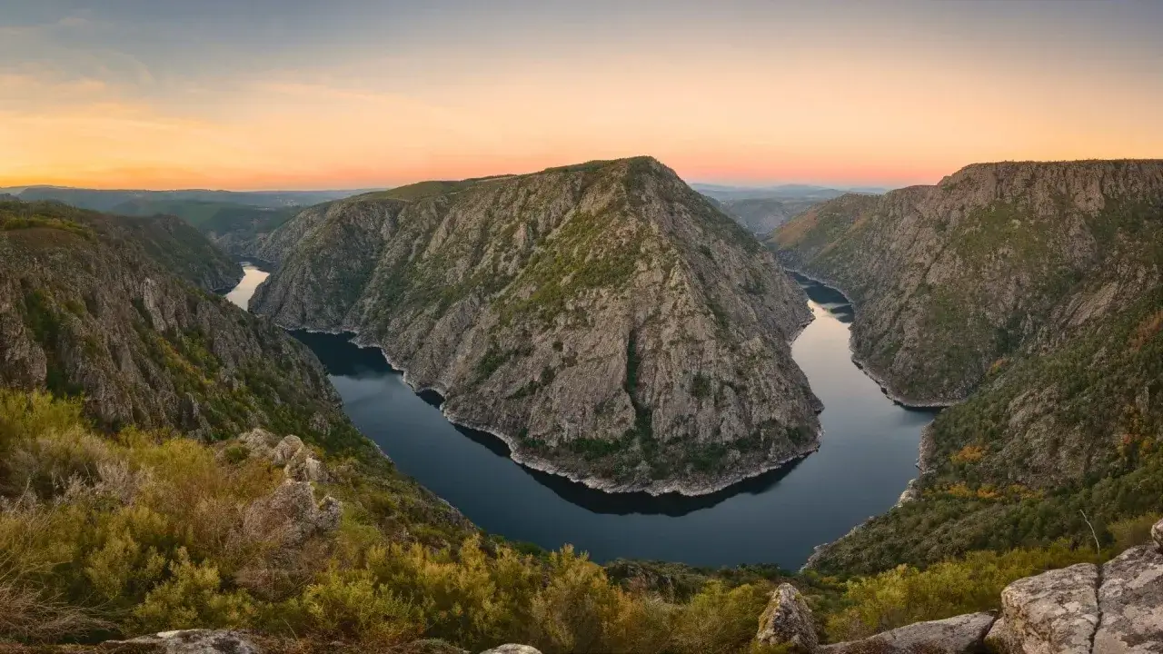 Majestuosos paisajes de Galicia con un río serpenteante entre montañas rocosas y vegetación otoñal al atardecer.