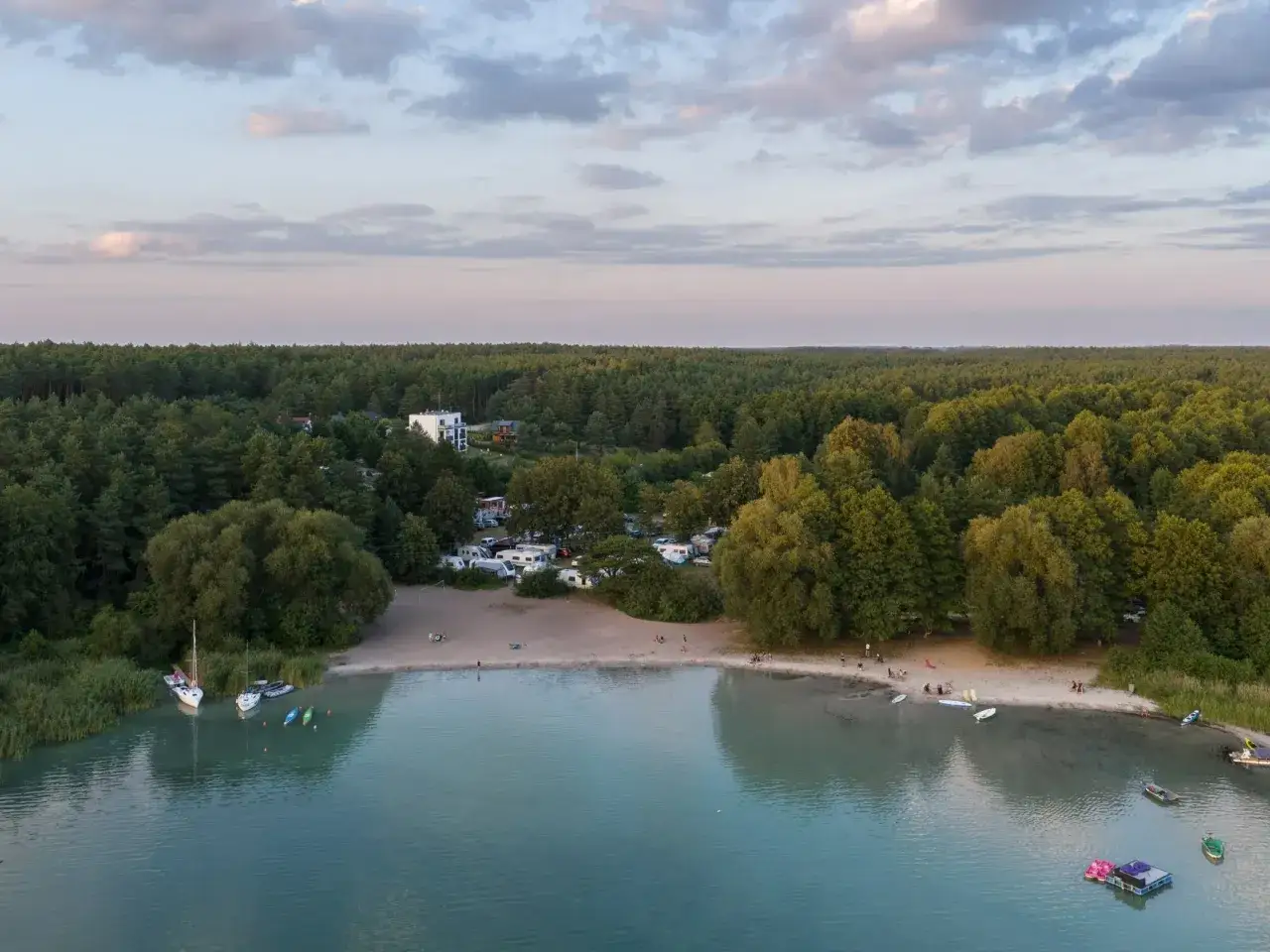 Widok na kemping nad najczystszym jeziorem w Polsce. Woda jest turkusowa, a brzeg piaszczysty. W oddali las.