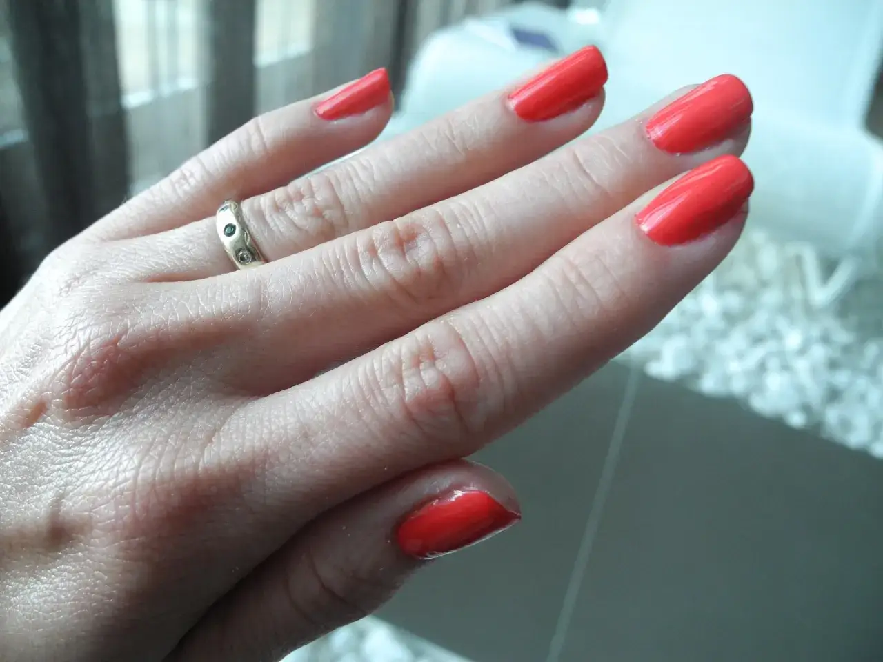 Dłoń z paznokciami pomalowanymi na jaskrawy koralowy kolor. Klasyczny manicure, który dodaje elegancji.