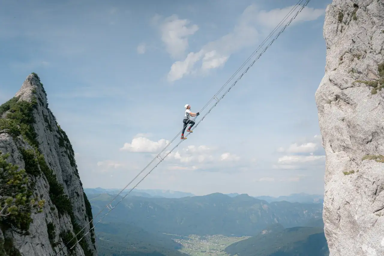 Osoba wspina się po drabinie na via ferrata w Austrii, podziwiając zapierające dech w piersiach widoki na g&oacute;ry i dolinę.