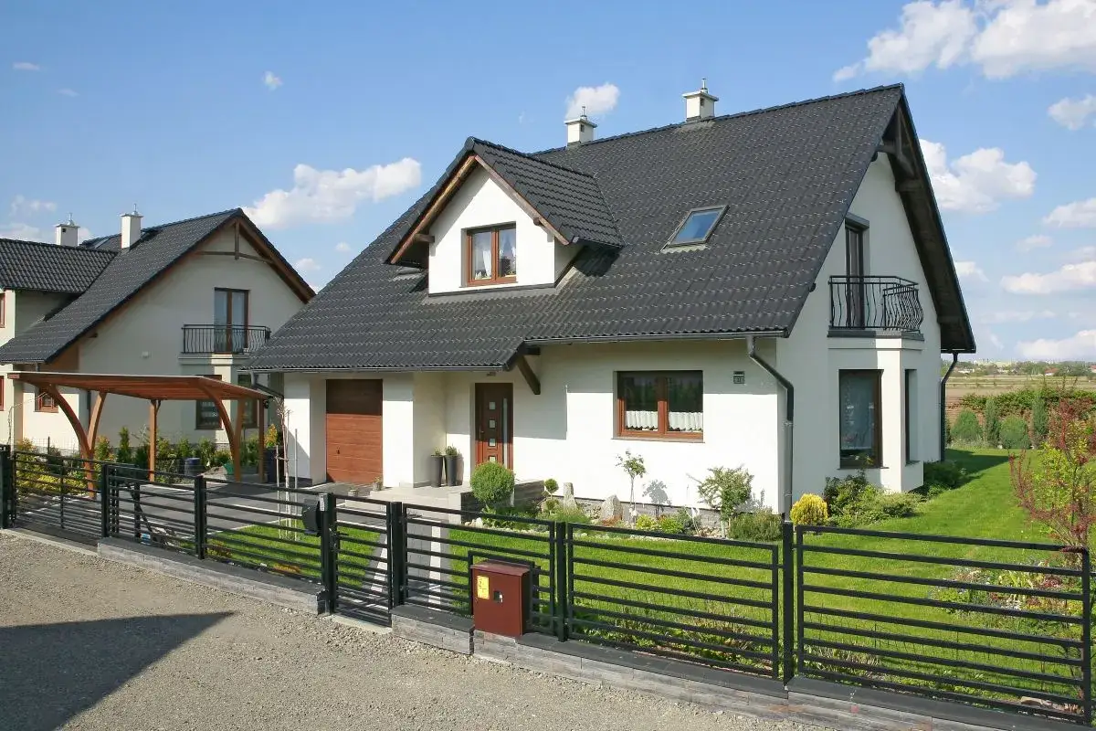 Nowoczesny dom z czarną dach&oacute;wką betonową Braas Celtycką, z drewnianą wiatą i zadbanym ogrodem.