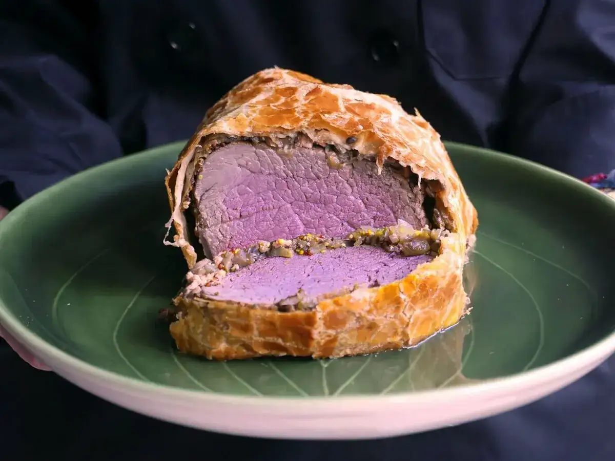 Un jugoso solomillo Wellington, perfectamente horneado, servido en un plato verde.