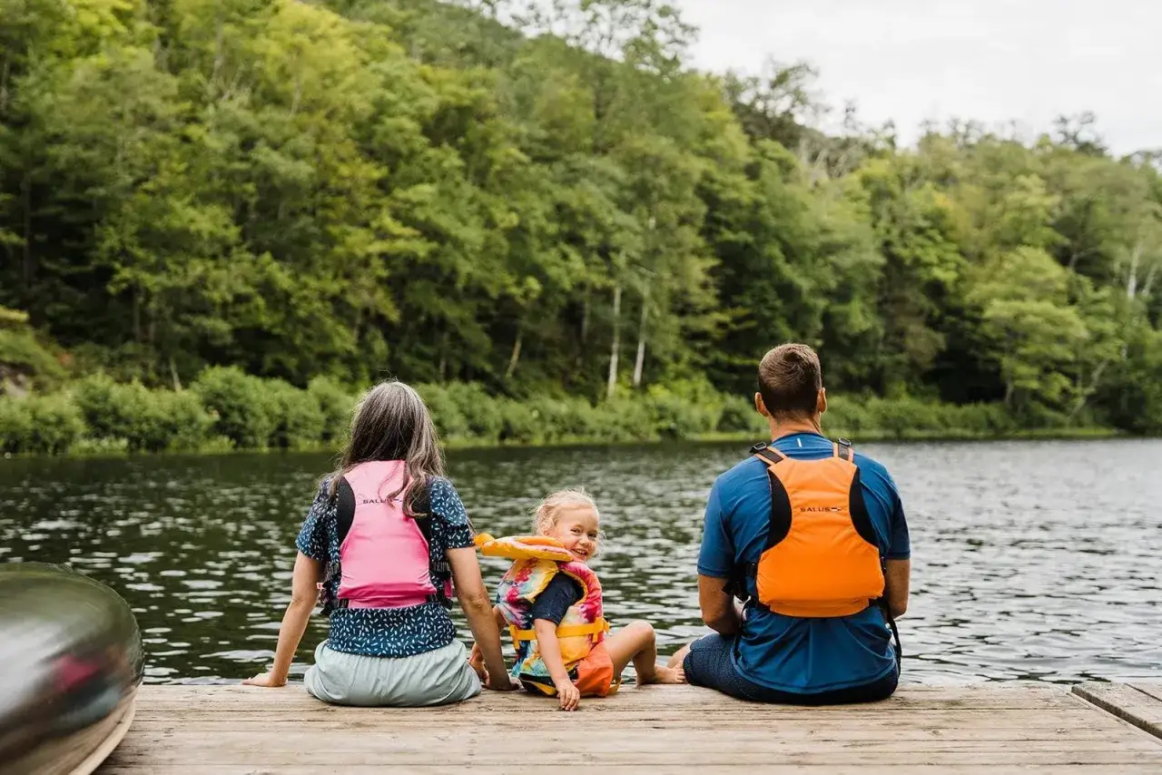 Famiglia in gita sul lago, Canada orientale con bambini. Un padre, una madre e una bambina con giubbotti salvagente siedono su un pontile.