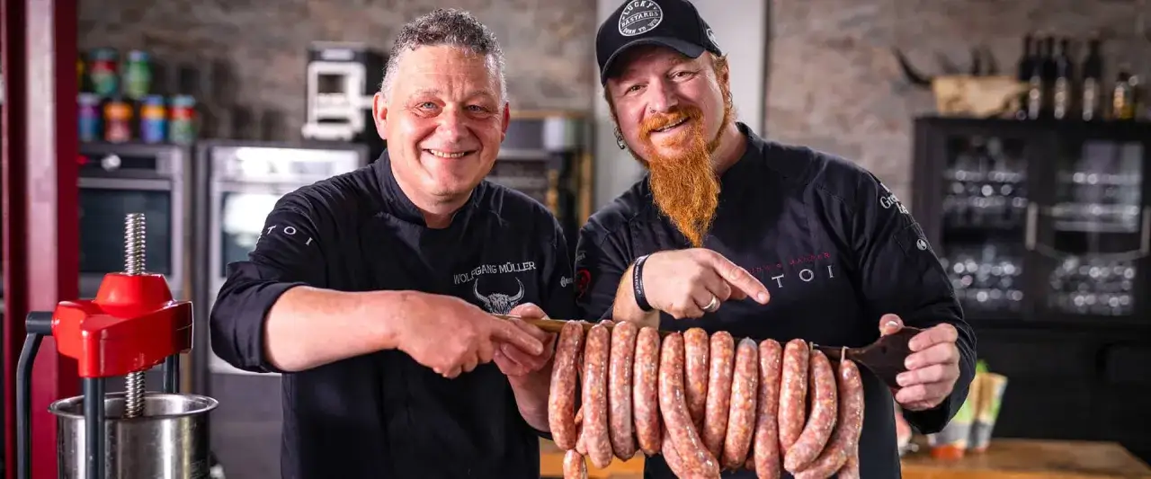 Zwei Metzger präsentieren stolz ihre frisch gemachten Würste. Sie zeigen, wie einfach es ist, salsiccia selber machen.