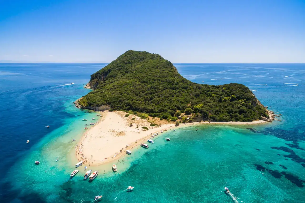 Malownicza wyspa grecka Zakynthos z piaszczystą plażą i turkusową wodą. Łodzie cumują przy brzegu, a na plaży wypoczywają turyści.