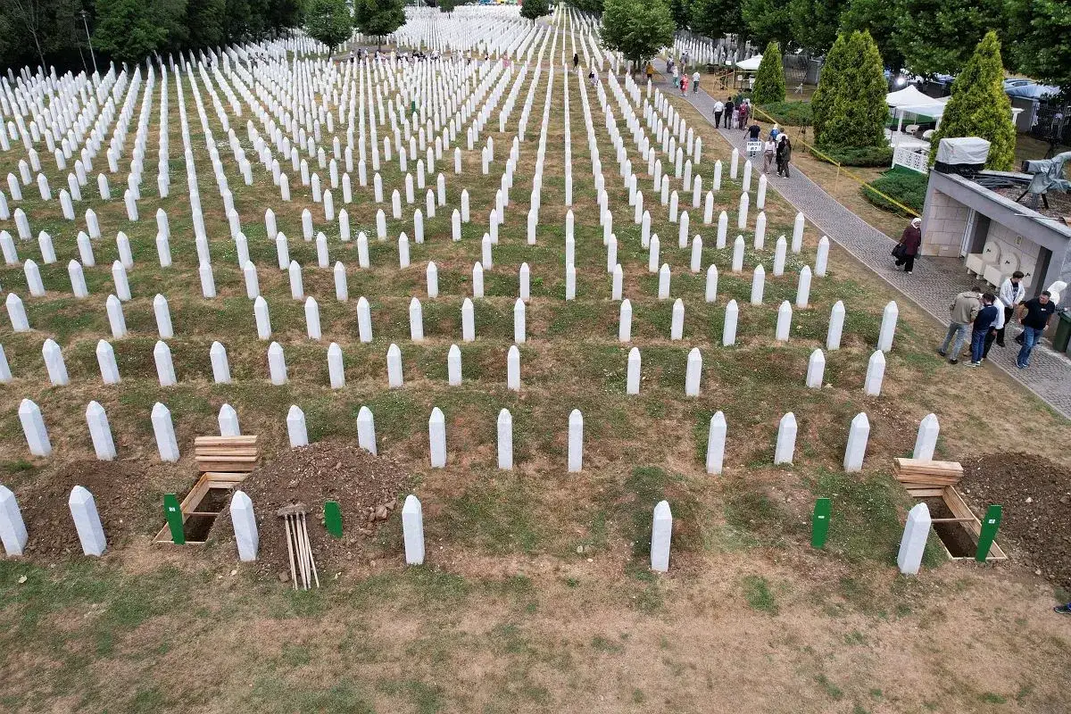 Cmentarz w Srebrenicy, rzędy białych nagrobków upamiętniają ofiary ludobójstwa. Widać świeżo wykopany grób.