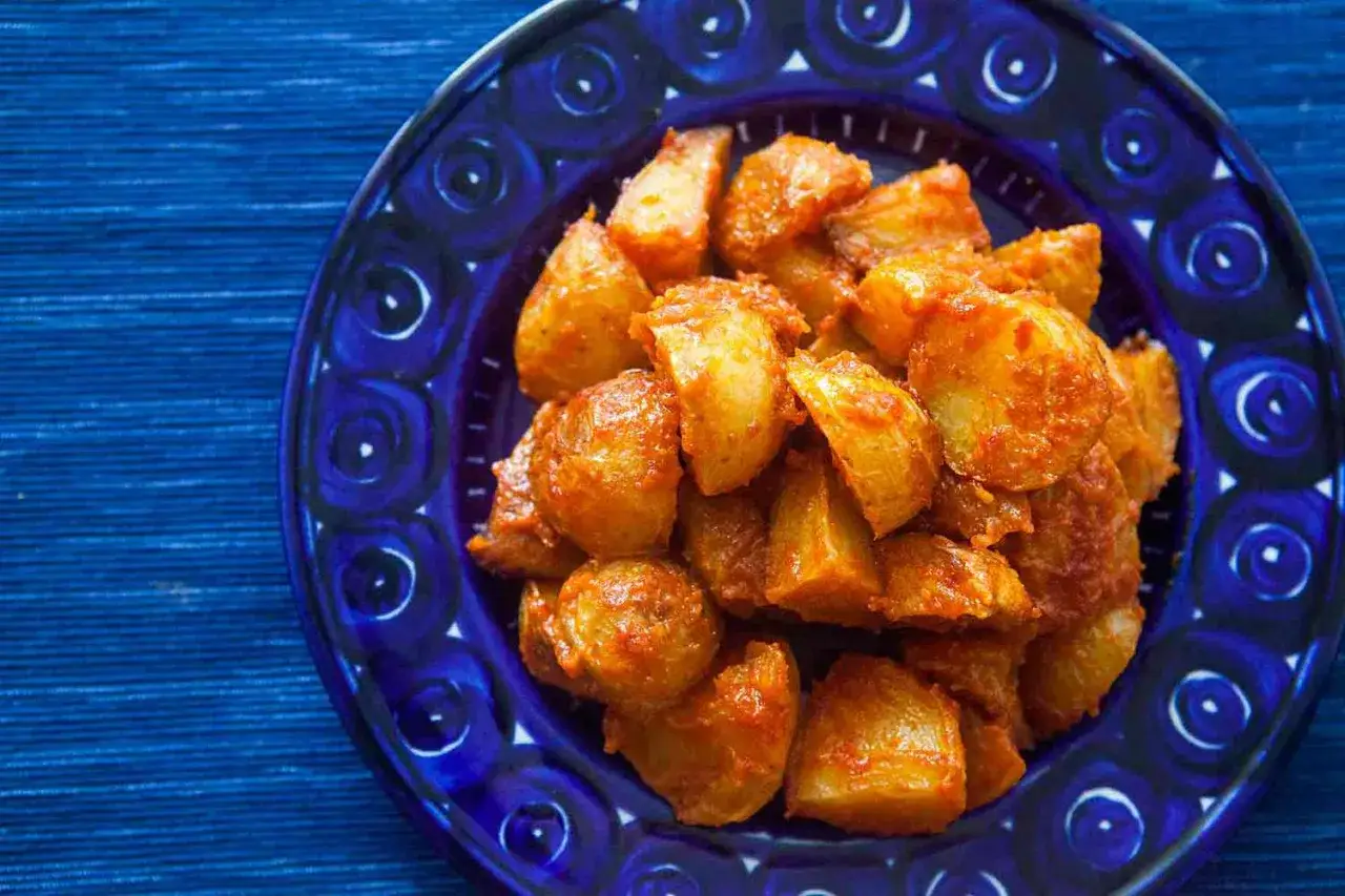 Patatas cortadas y cubiertas con una sabrosa salsa brava, servidas en un plato azul decorado.