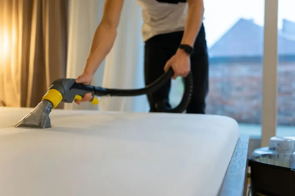 Persona usando un limpiador de tapicer&iacute;a para limpiar un colch&oacute;n. Aprende c&oacute;mo limpiar colchones en casa para un descanso m&aacute;s saludable.