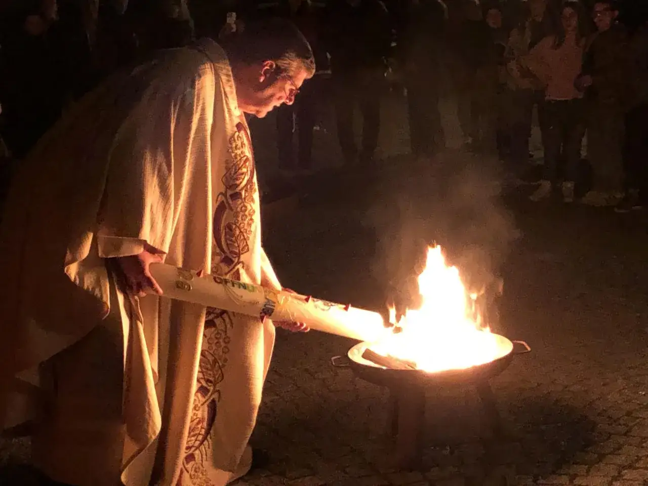Priester entz&uuml;ndet Osterkerze bei einem feierlichen Osternacht Gottesdienst. Menschen stehen im Dunkeln und beobachten das Licht.