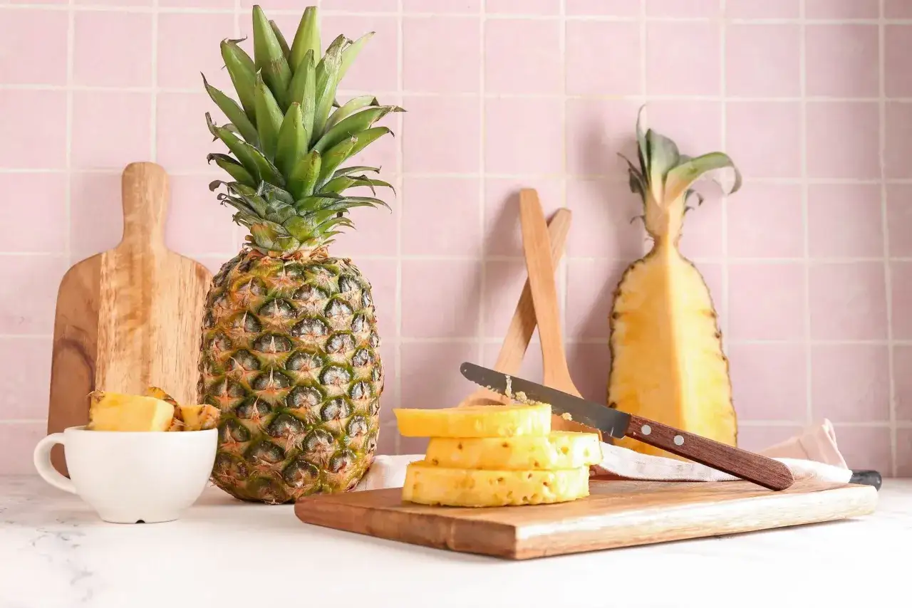 Ananas pokrojony w plastry na desce, obok cały owoc i połówka. Warto sprawdzić ananas indeks glikemiczny przed spożyciem.