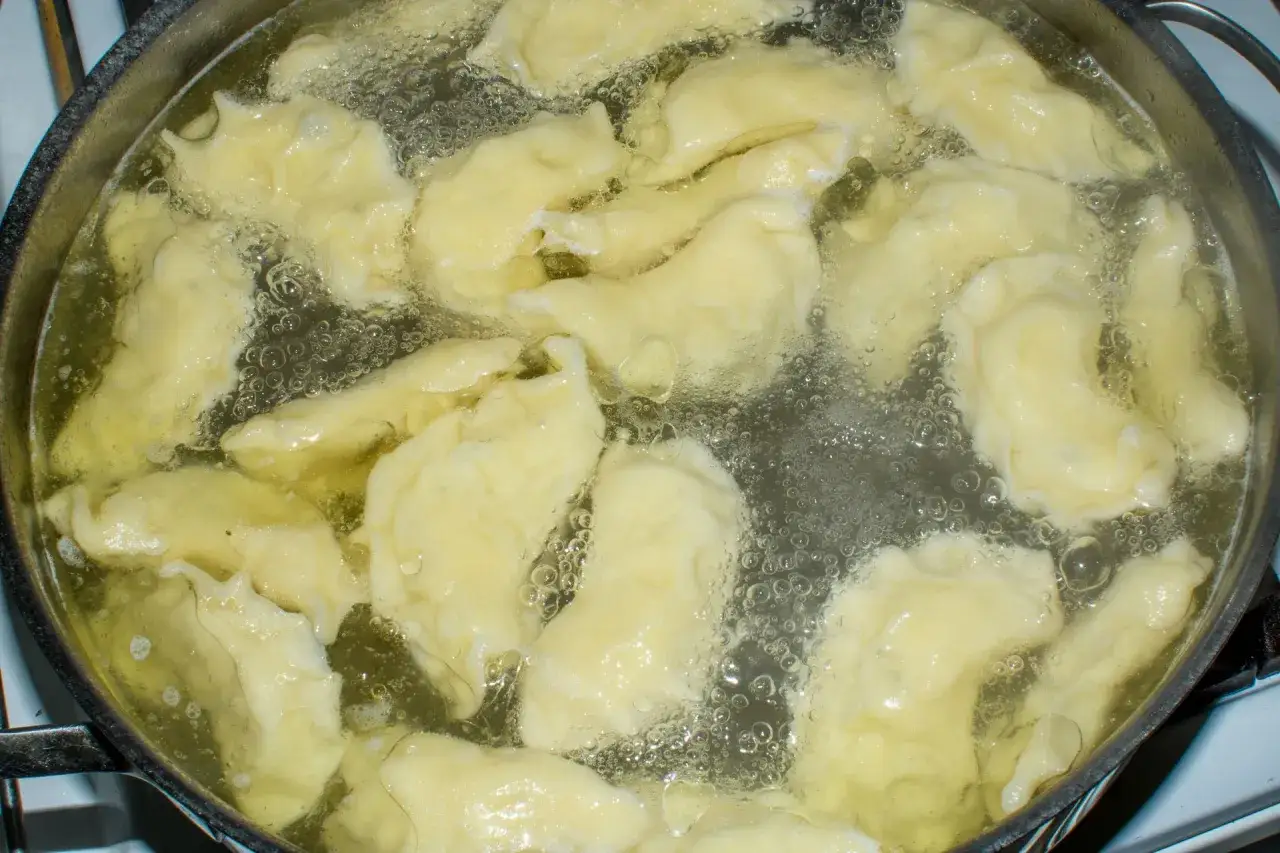 Gotowane pierogi unoszą się w bulgoczącej wodzie. To świetny sposób, by dowiedzieć się, jak mrozić ugotowane pierogi na później.