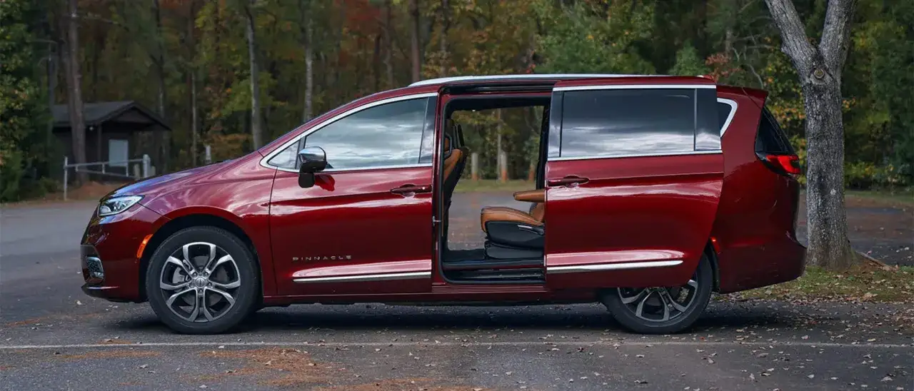 Czerwony Chrysler Pacifica Pinnacle z otwartymi drzwiami, ukazujący wnętrze. Wymiary tego przestronnego minivana zapewniają komfort podróży.