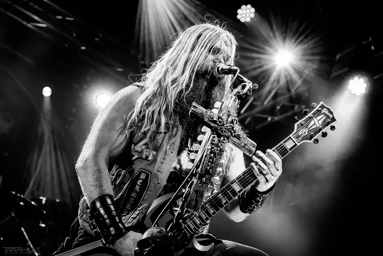 Karol Makurat, wokalista z długimi włosami i brodą, gra na gitarze Gibson podczas koncertu.