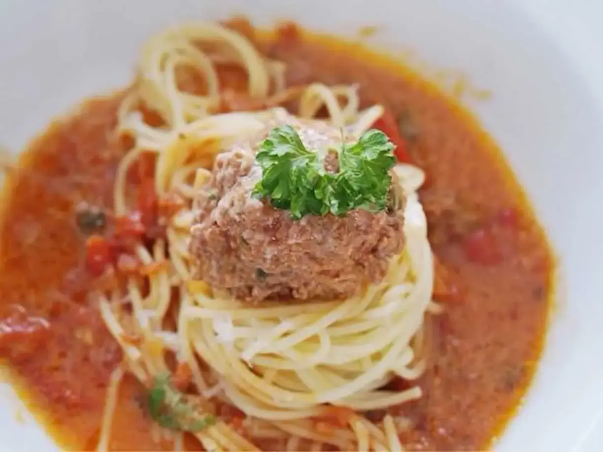En portion spaghetti med en stor k&ouml;ttbulle toppad med persilja, serverad i en kr&auml;mig tomats&aring;s.