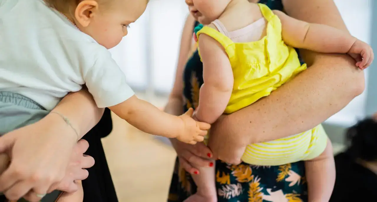 Deux bébés se tiennent la main, l'un en blanc, l'autre en jaune. L'un semble vouloir s'accrocher, signe d'angoisse de séparation.