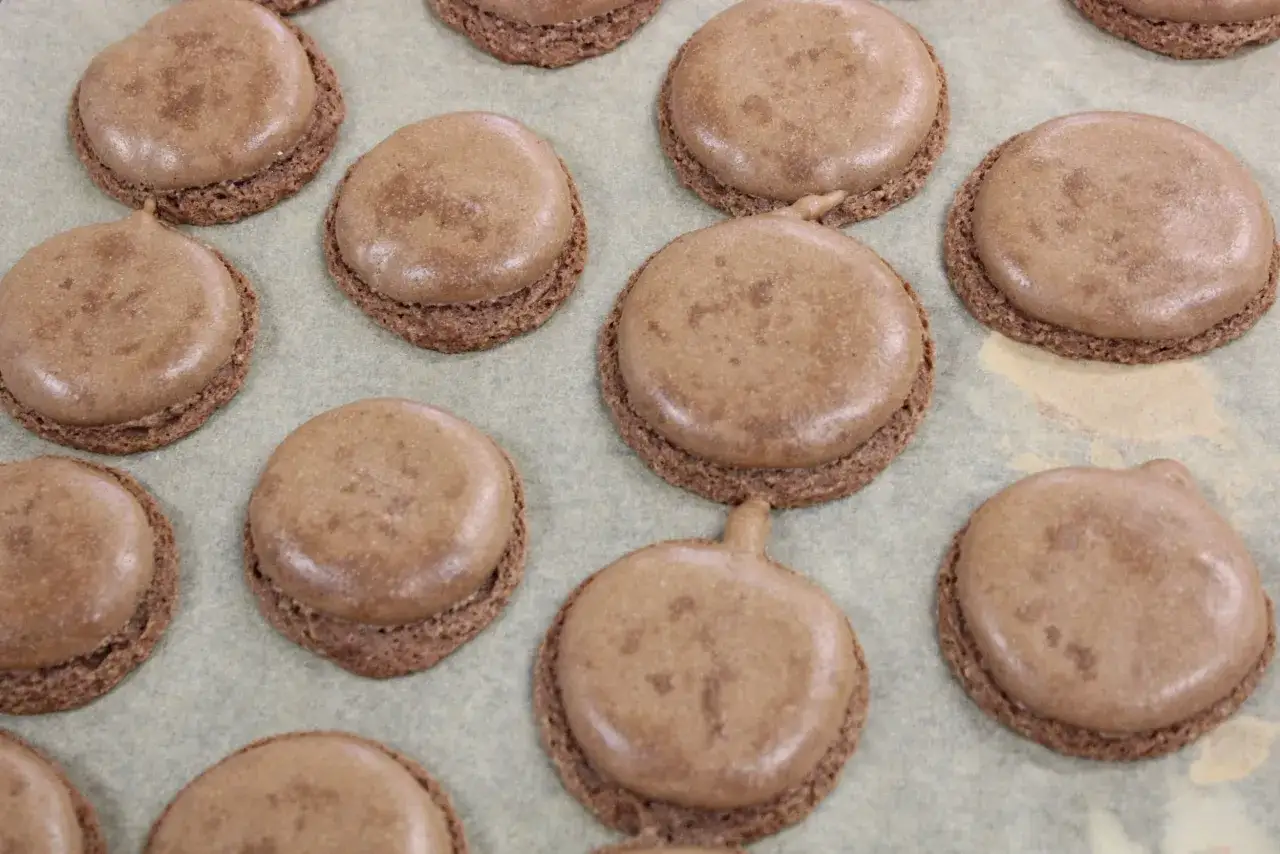 Des macarons au chocolat sur une plaque. Certains ont des pieds craquel&eacute;s, expliquant pourquoi mes macarons craquent.