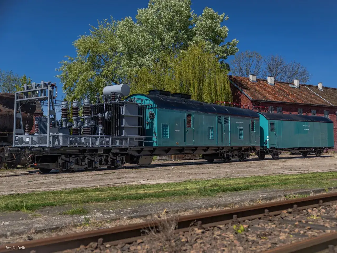 Zielony wagon kolejowy z transformatorem, który może pomóc zrozumieć, ile prądu zużywa pociąg.