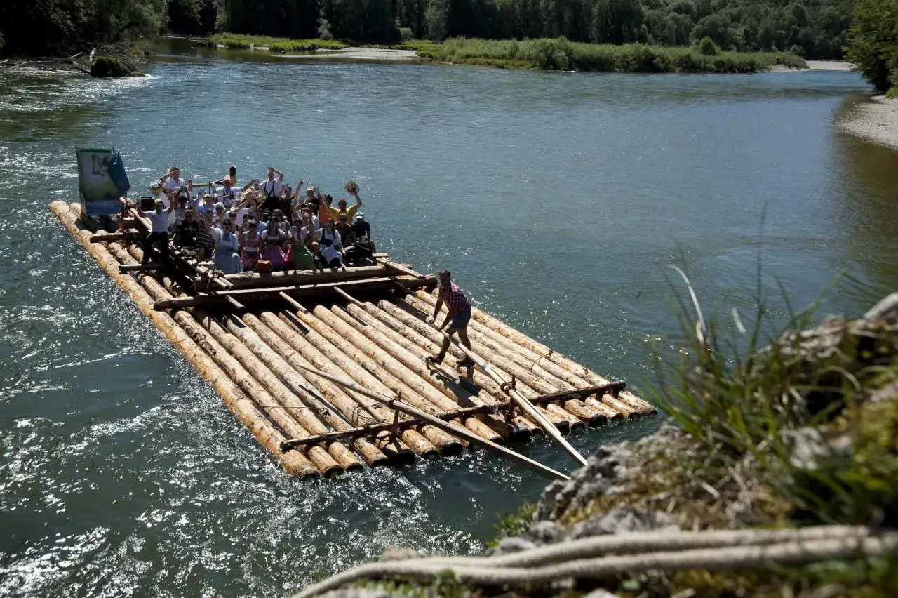 Fröhliche Menschen auf einem Floß treiben auf einem Fluss. Ein Mann steuert das Floß mit Stangen.