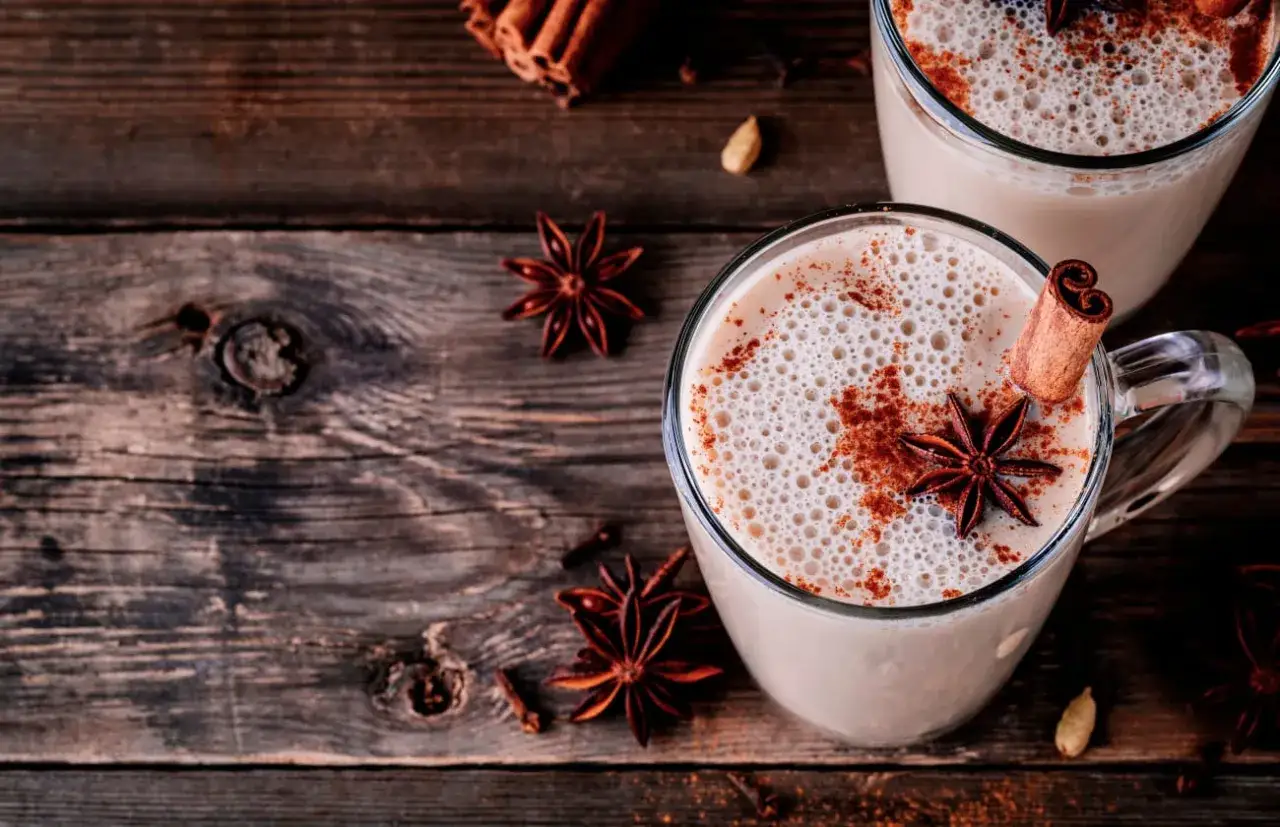 Deux tasses de lait de poule crémeux, garnies de cannelle et d'anis étoilé, sur une table en bois rustique.