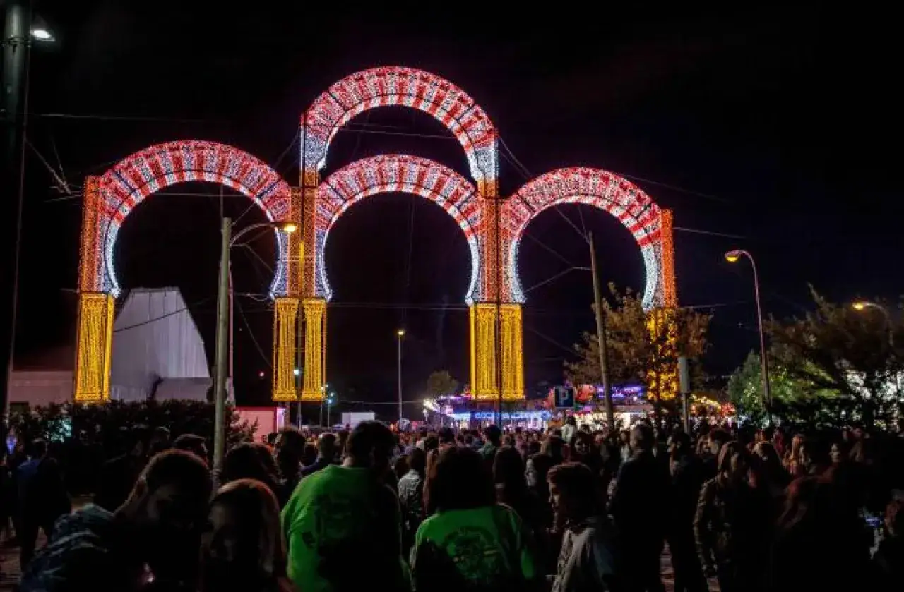 Noche de luces y alegría en las fiestas de Boadilla del Monte. Arcos luminosos decoran la multitud que celebra.