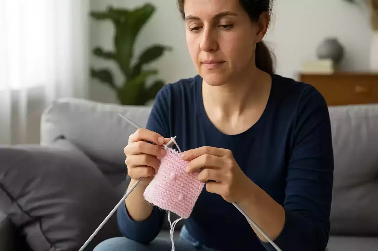 Mujer tejiendo un delicado punto viborita en lana rosa.