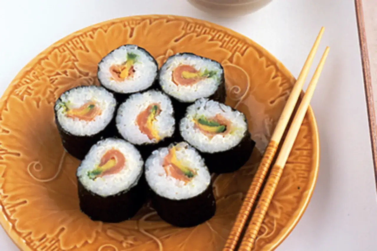 Pyszne domowe sushi z łososiem i awokado na ozdobnym talerzu, obok pałeczki.