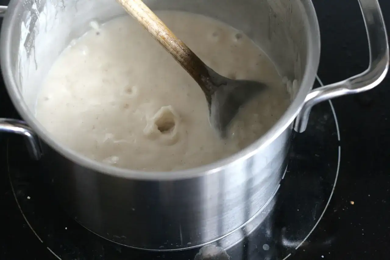 Ein Holzlöffel rührt in einem Topf mit cremigem Milchreis, der gerade köchelt. Dieser weltbester Milchreis wird sicher köstlich!