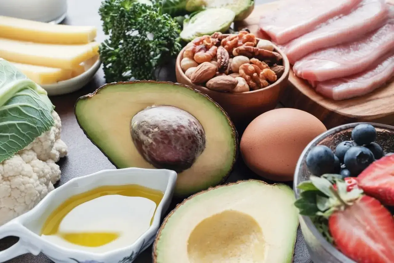 Na talerzu składniki na dietę keto: awokado, jajko, orzechy, ser, mięso, jagody, truskawki, brokuły, kalafior i oliwa.