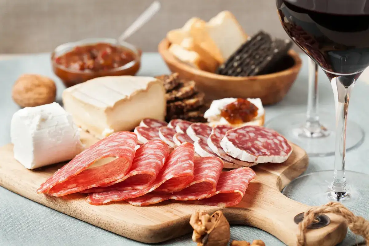 Un verre de vin rouge accompagne un plateau de charcuterie, fromages, pain et confiture. Parfait pour un apéro !