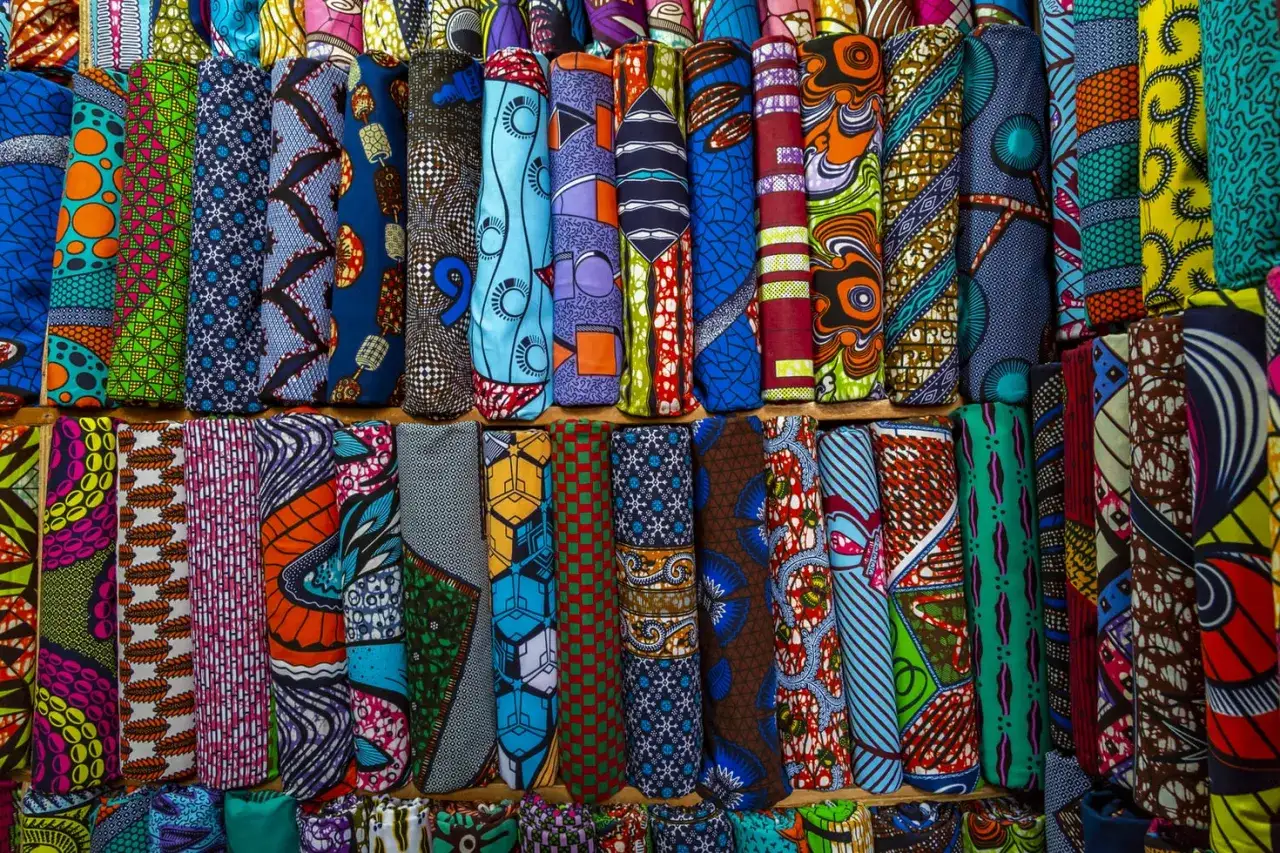 A vibrant display of rolled ankara fabric, showcasing bold geometric and abstract patterns in a rainbow of colors.