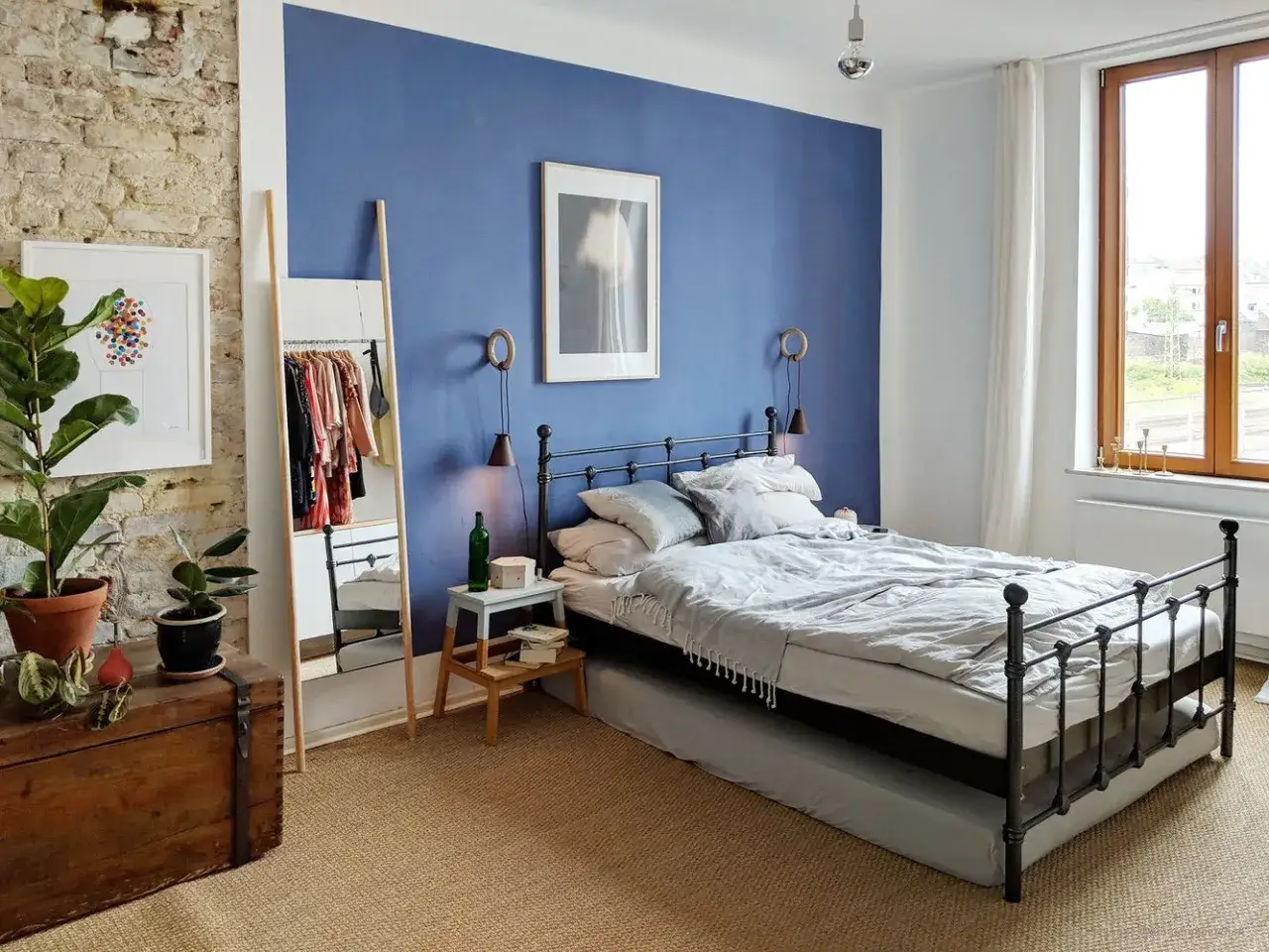 Ein Schlafzimmer mit einem blauen Bett und einer auffälligen blauen Wandfarbe. Ein Spiegel und Kleidung stehen neben dem Bett.