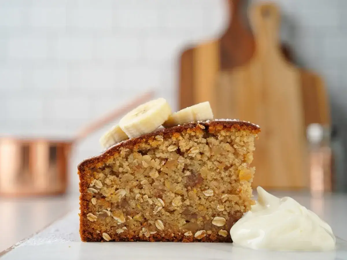 Tranche de gâteau banane flocon d'avoine, garnie de rondelles de banane et d'une cuillère de crème. Parfait pour une recette saine.