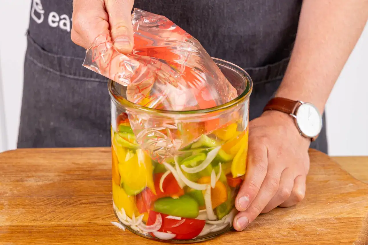Bunte Paprikast&uuml;cke und Zwiebeln werden in einem Glas f&uuml;r das Paprika fermentieren vorbereitet. Ein Plastikbeutel wird &uuml;ber das Gem&uuml;se gelegt.