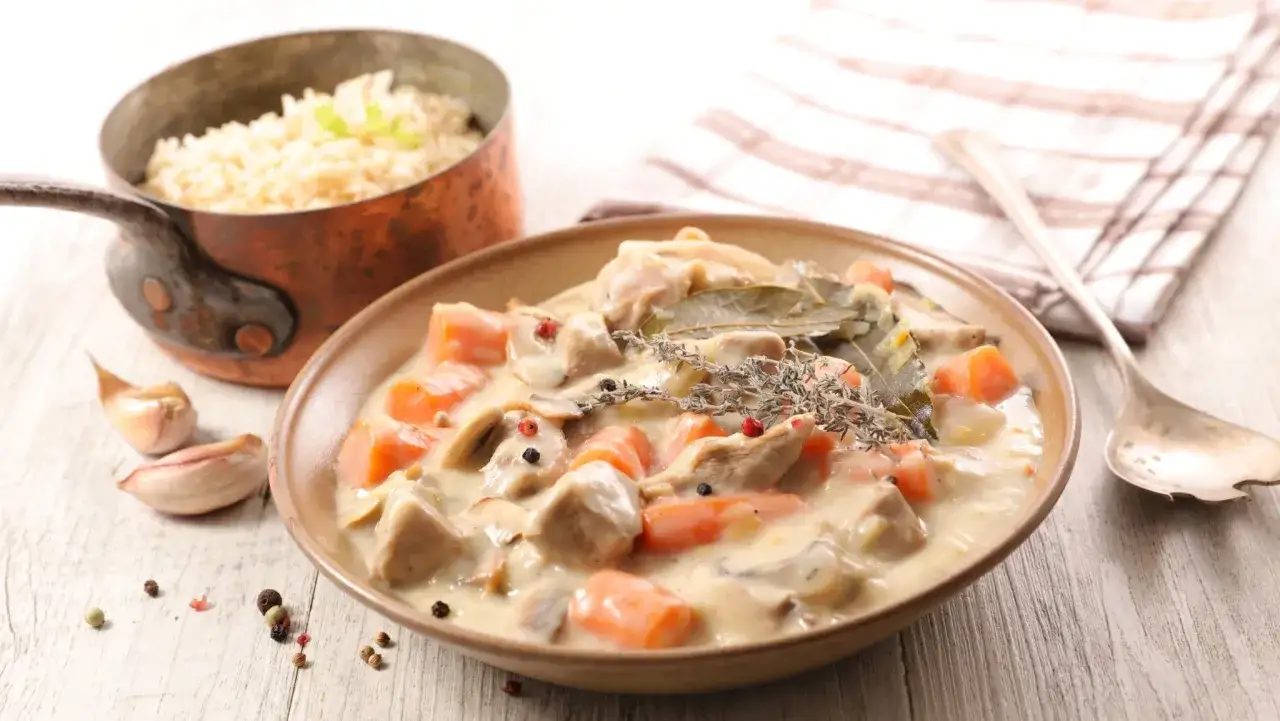 Un plat de blanquette de veau crémeuse avec carottes et champignons, servi avec du riz. Un verre de vin rouge est suggéré pour accompagner ce délice.