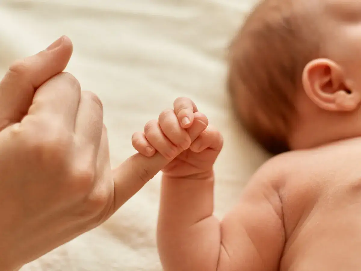 El descubrimiento de las manos de los bebés es un momento tierno. Una mano adulta sostiene el pequeño dedo de un recién nacido, un vínculo especial.