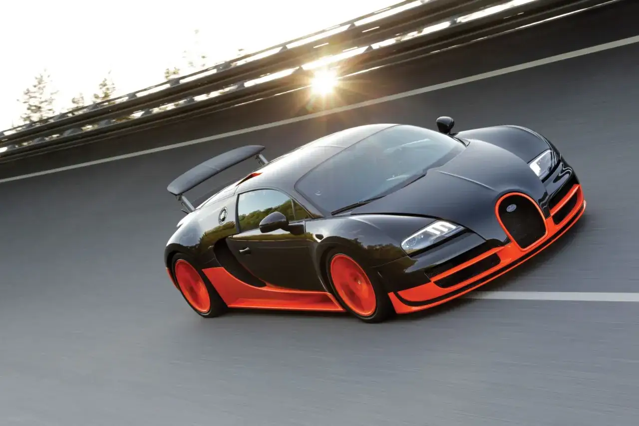 Czarny Bugatti Veyron z pomarańczowymi akcentami pędzi po autostradzie, słońce przebija się przez chmury.