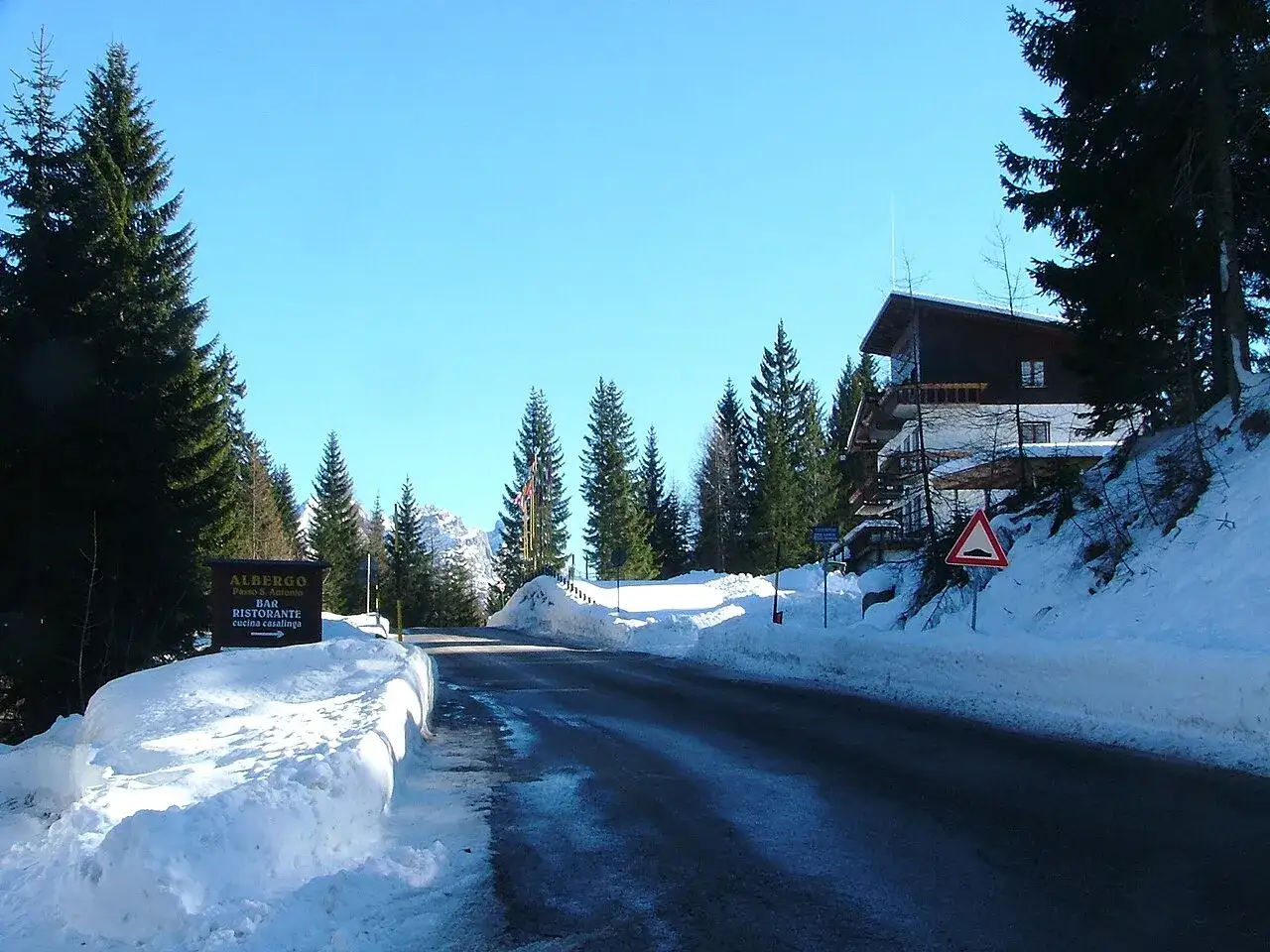 Strada innevata al Passo San Antonio, con un albergo e un cartello che indica
