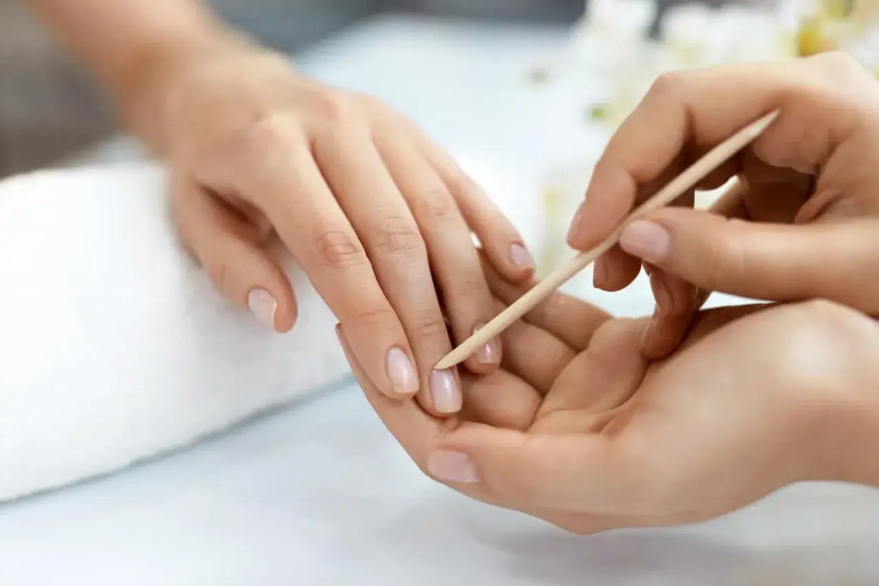 Delikatne dłonie poddawane zabiegowi manicure biologiczny. Drewniany patyczek delikatnie odsuwa skórki, przygotowując paznokcie do pielęgnacji.