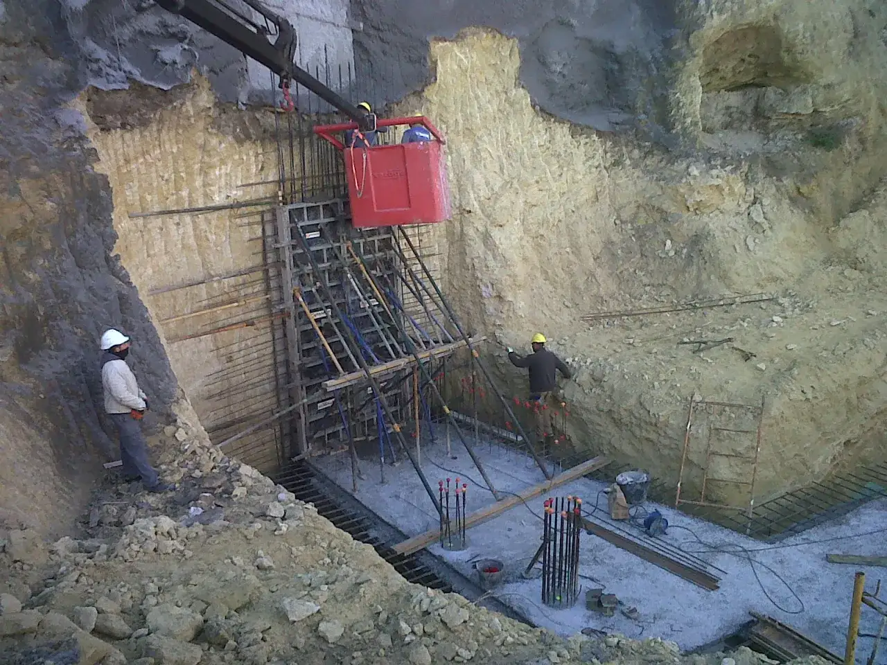 Trabajadores en una excavación por bataches, con encofrados y armaduras de acero preparadas para hormigonar.